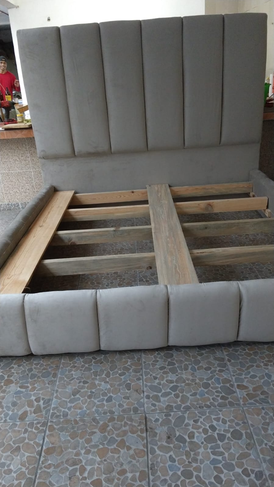 Cama con cabecera tapizada en canesú gris, en fabricación