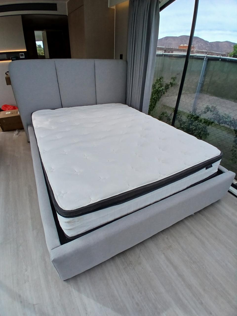 Cabecera tapizada gris con colchón, vista lateral en recámara