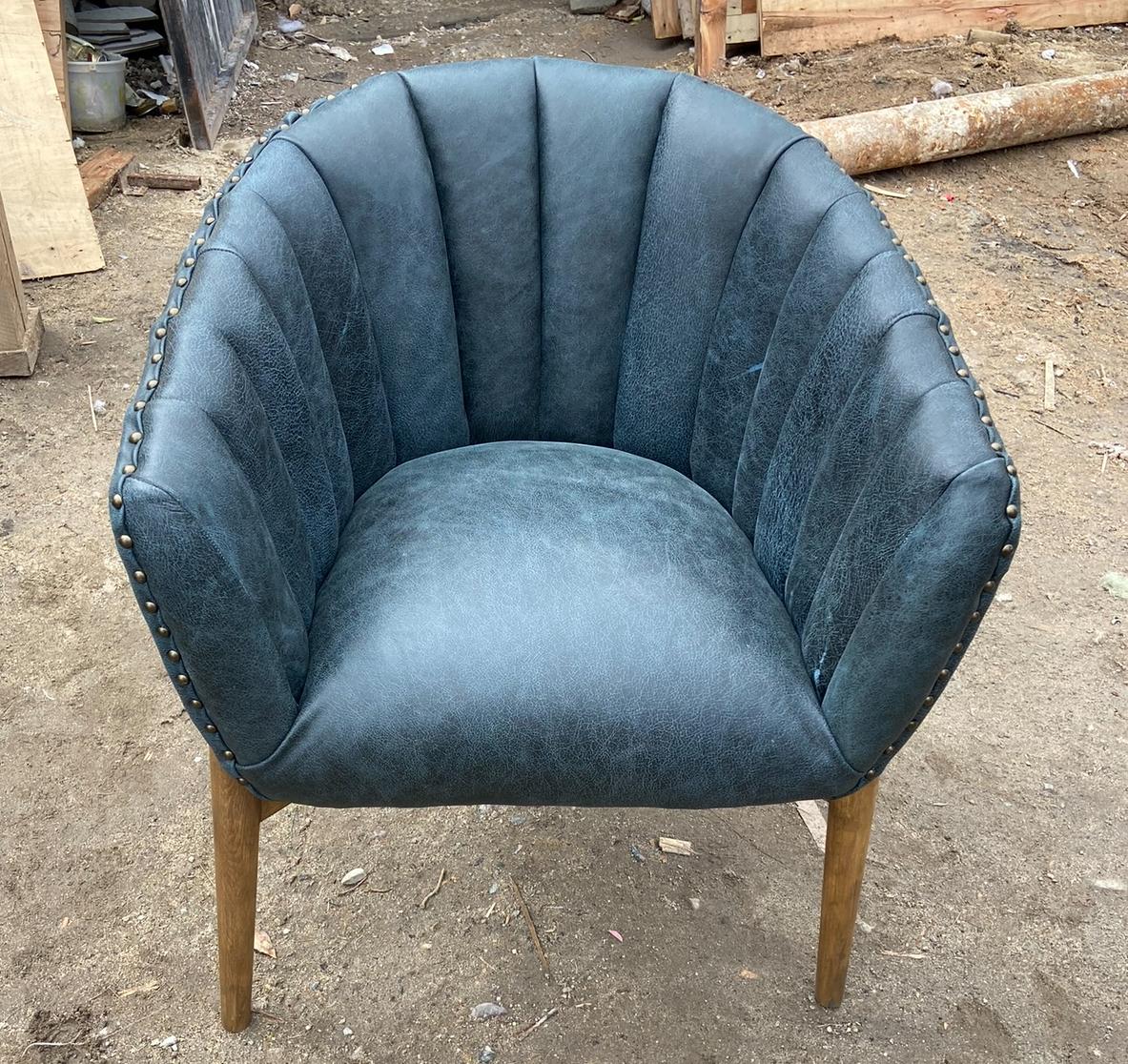 Sillón tipo concha tapizado en piel azul petróleo con tachuelas
